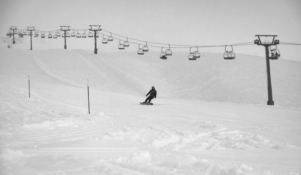 man-snowboarding-below-cable-carts-during-day-2421019